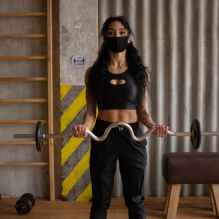 sportswoman in mask training with weights in gym